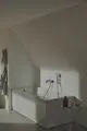 Weiße Badewanne in einem minimalistisch gestalteten Badezimmer, mit einer Ideal Standard Brausearmatur und einer Übersicht von Pflegeprodukten auf einem kleinen Beistelltisch.